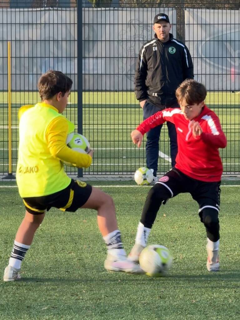 Spieler von Rot-Weiss Essen und Borussia Dortmund im intensiven 1-gegen-1-Duell während des Elite-Duo-Trainings der Edin Husic Fußballschule. Der Trainer beobachtet die Szene, um präzises Feedback zu geben.