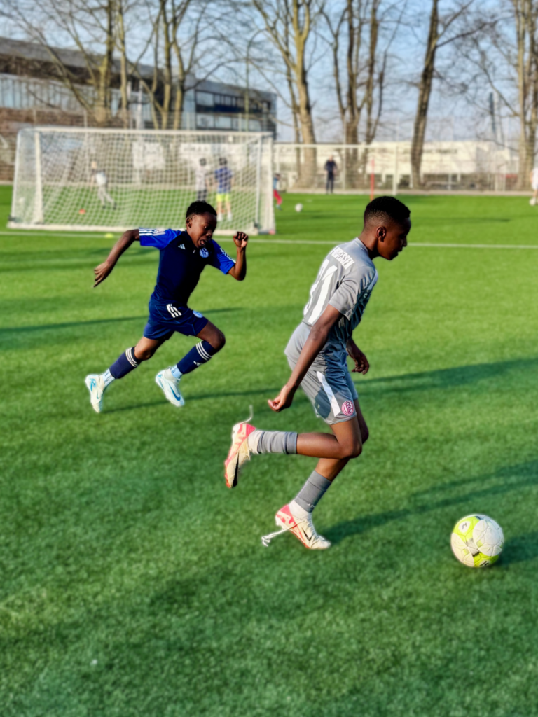 Zwei junge Fußballtalente im intensiven Zweikampf auf dem Spielfeld. Dynamik, Schnelligkeit und Spielintelligenz sind die Schlüssel zum Erfolg im modernen Fußball.
